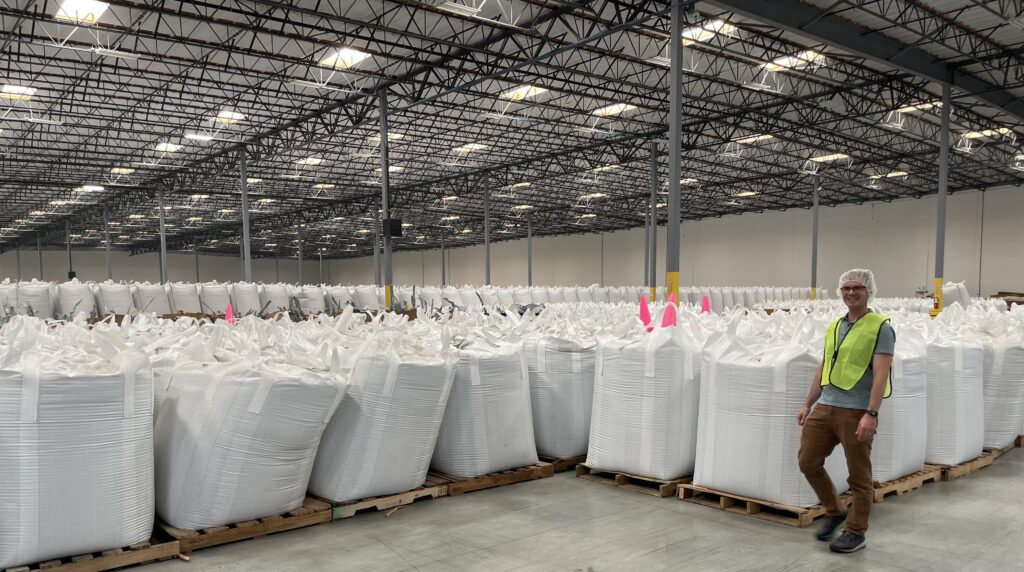 Man in front of large white bags of recycled plastic pellets