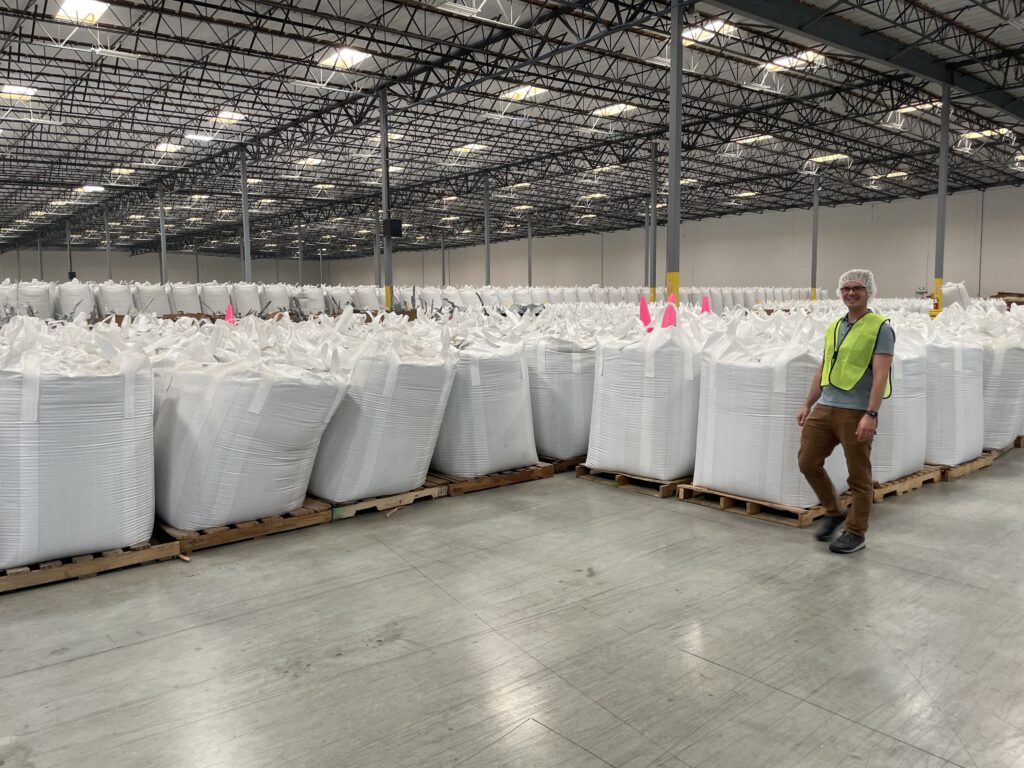 Man in front of large white bags of recycled plastic pellets