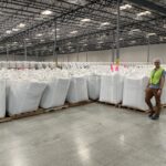 Man in front of large white bags of recycled plastic pellets