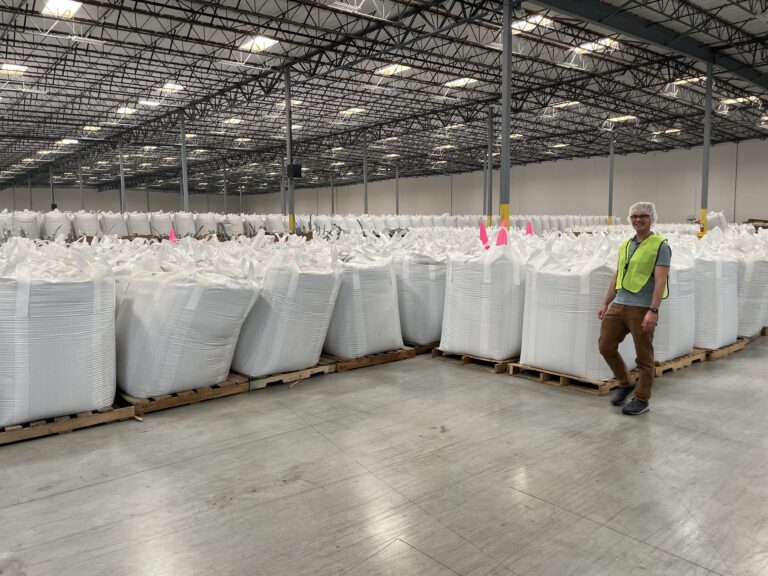 Man in front of large white bags of recycled plastic pellets
