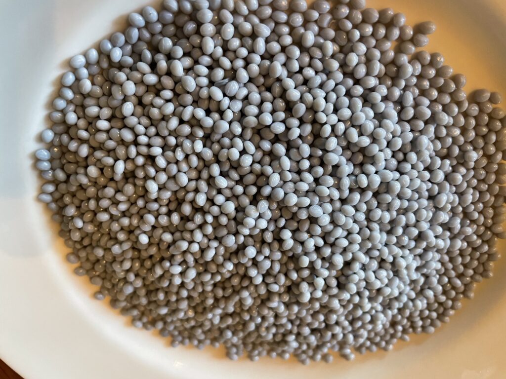 A small bowl of bluish, rice-sized plastic pellets, made with recycled plastic